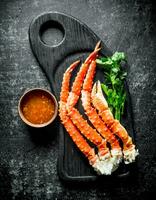 Crab on a cutting Board with greens and sauce in a bowl. photo