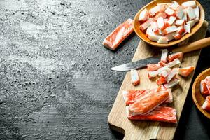 Pieces of crab sticks on a wooden cutting Board with a knife. photo