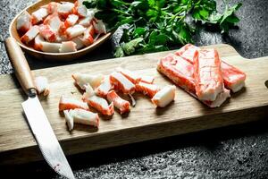 Pieces of crab sticks on a cutting Board and a plate of parsley. photo