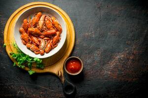 Boiled crayfish in a bowl on a cutting Board with parsley and sauce. photo