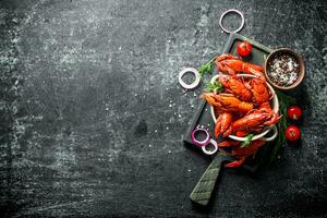 hervido cangrejo de río en un corte tablero con cebolla anillos, Tomates y especias foto