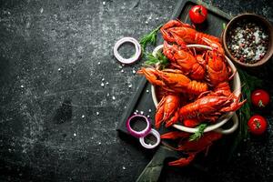 Boiled crayfish on a cutting Board with onion rings, tomatoes and spices. photo