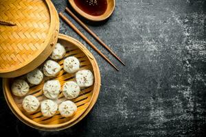 Fragrant manta dumplings in a bamboo steamer with soy sauce in a plate. photo