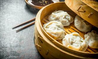 Hot aromatic manta dumplings in bamboo steamer with soy sauce. photo