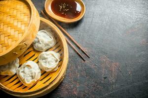 Hot aromatic manta dumplings in bamboo steamer with soy sauce. photo