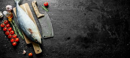 Raw fish on a cutting Board with rosemary, tomatoes and garlic. photo