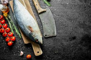 Raw fish on a cutting Board with a knife, tomatoes and garlic. photo