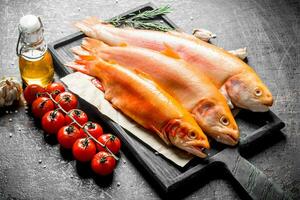 crudo trucha en un corte tablero con Tomates, Romero y ajo clavos de olor. foto