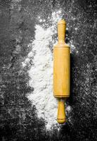 Wheat flour with rolling pin on rustic background. photo