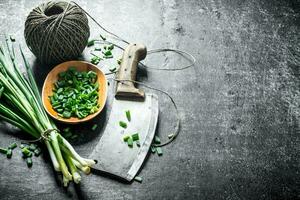 Bunch of green onion with chopped green onion on a plate, old knife and twine. photo