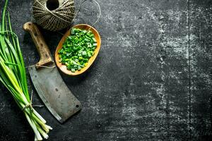 Bunch of green onion with chopped green onion on a plate, old knife and twine. photo