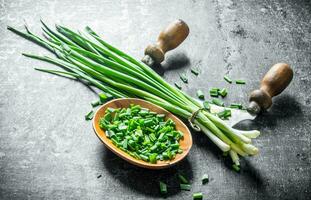 Chopped green onion in a wooden plate with a knife. photo