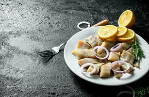 Pieces of salted herring on a plate with sliced lemon and onion. photo