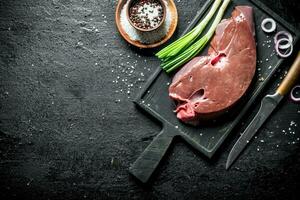 Raw liver on a cutting Board with a knife, spices and onions. photo