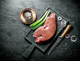 Raw liver on a cutting Board with a knife, spices and onions. photo
