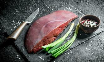 Raw liver on a stone Board with green onions and spices. photo