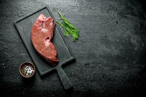 Piece of raw liver on a cutting Board with dill and spices. photo