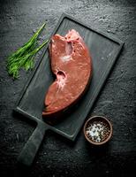 Piece of raw liver on a cutting Board with dill and spices. photo