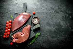 Raw liver on a cutting Board with spices, cherry tomatoes and dill. photo