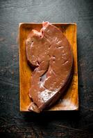 Piece of raw liver on a wooden plate. photo