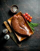 Piece of raw liver on a plate with a knife, spices and tomatoes on a branch. photo