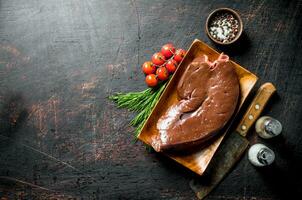 Piece of raw liver on a plate with a knife, spices and tomatoes on a branch. photo