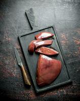 Pieces of raw liver with a knife on the cutting Board. photo