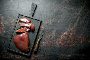 Pieces of raw liver with a knife on the cutting Board. photo