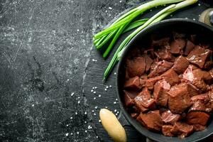 Pieces of raw liver in a saucepan with green onions. photo