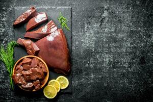 Pieces of raw liver on a stone Board with pieces of lemon. photo