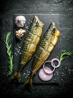 Fragrant smoked fish mackerel on a stone Board with onion rings, rosemary and garlic. photo