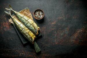 Appetizing smoked mackerel on paper with spices in bowl. photo