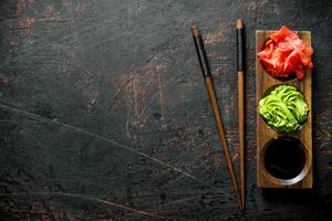 Soy sauce, ginger and wasabi on a wooden stand with chopsticks. photo