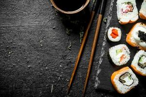 Delicious rolls with salmon and vegetables on a stone Board with soy sauce in bowl. photo