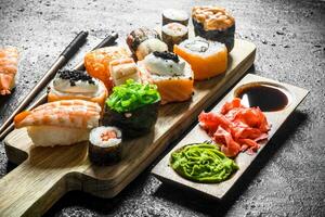 Sushi rolls with salmon and vegetables on a cutting Board with sauce and chopsticks. photo