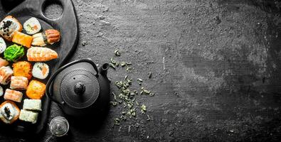 Pieces of delicious sushi rolls on the cutting Board with tea in the teapot. photo