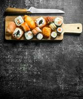 Various Japanese sushi rolls on wooden cutting Board with knife. photo