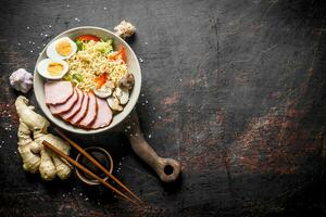 Instant noodles in bowl with ham, vegetables and egg on cutting Board. photo