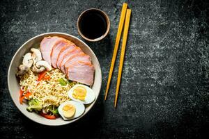 Instant noodles with vegetables, egg, ham, soy sauce and chopsticks. photo