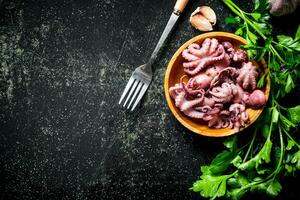 Baby octopus on a plate with parsley and garlic cloves. photo