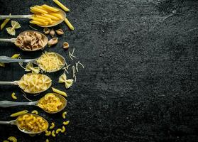 Different types of dry pasta in spoons. photo