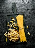 Different types of dry pasta on a cutting Board and a bowl. photo