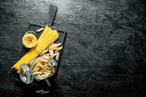 Assortment of different types of pasta dry on a cutting Board and in a glass jar. photo