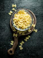 Dry Farfalle pasta in a glass bowl on a cutting Board. photo