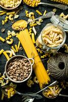 Pasta background. Assortment of different types of dry pasta in bowl and spoons with twine. photo