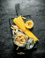 Assortment of different types of pasta dry on a cutting Board and in a glass jar. photo