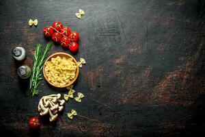 Raw Farfalle pasta in a bowl with the tomatoes, rosemary, mushrooms and spices. photo