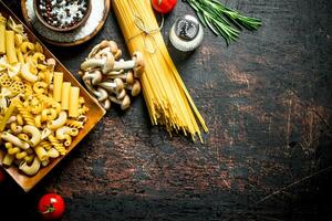 Different types of raw pasta with tomatoes, spices and mushrooms. photo