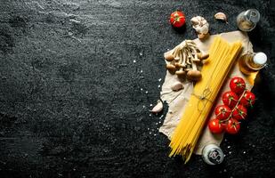 Raw spaghetti on paper with mushrooms, spices and tomatoes on a branch. photo