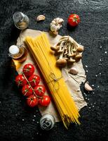 Raw spaghetti on paper with mushrooms, spices and tomatoes on a branch. photo